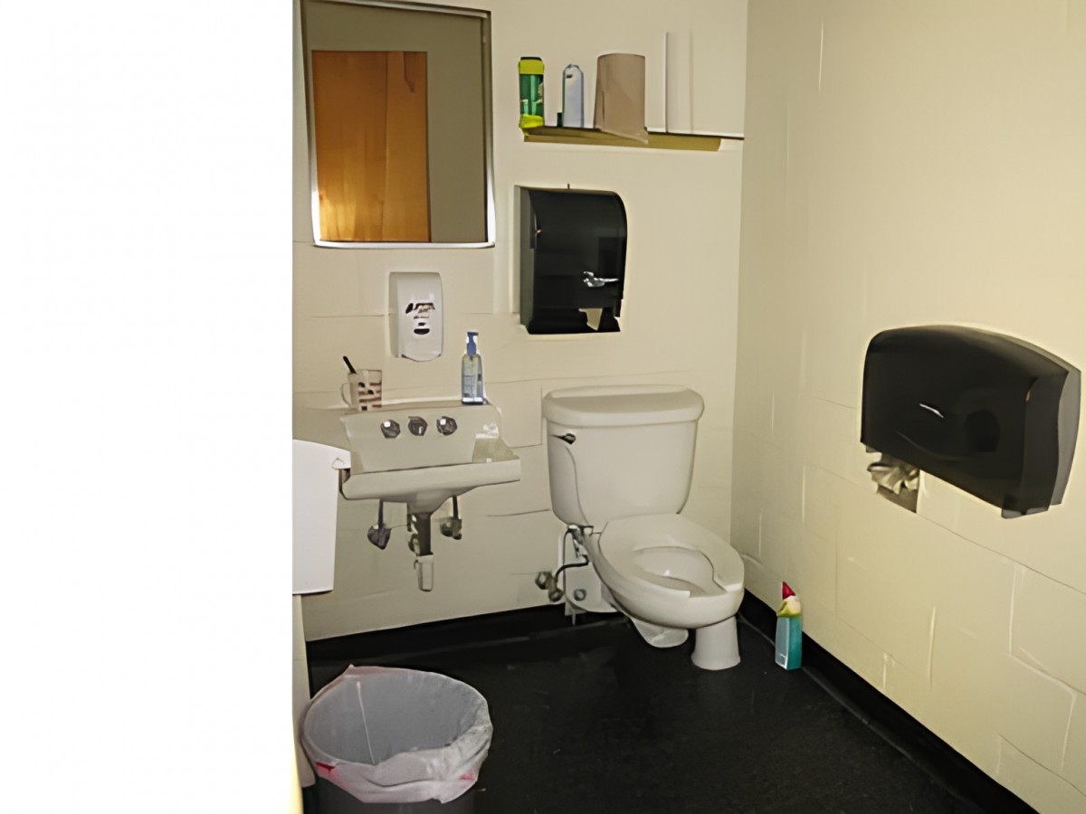 A small restroom with essential facilities, including a toilet, sink, mirror, and dispensers for soap and paper towels.