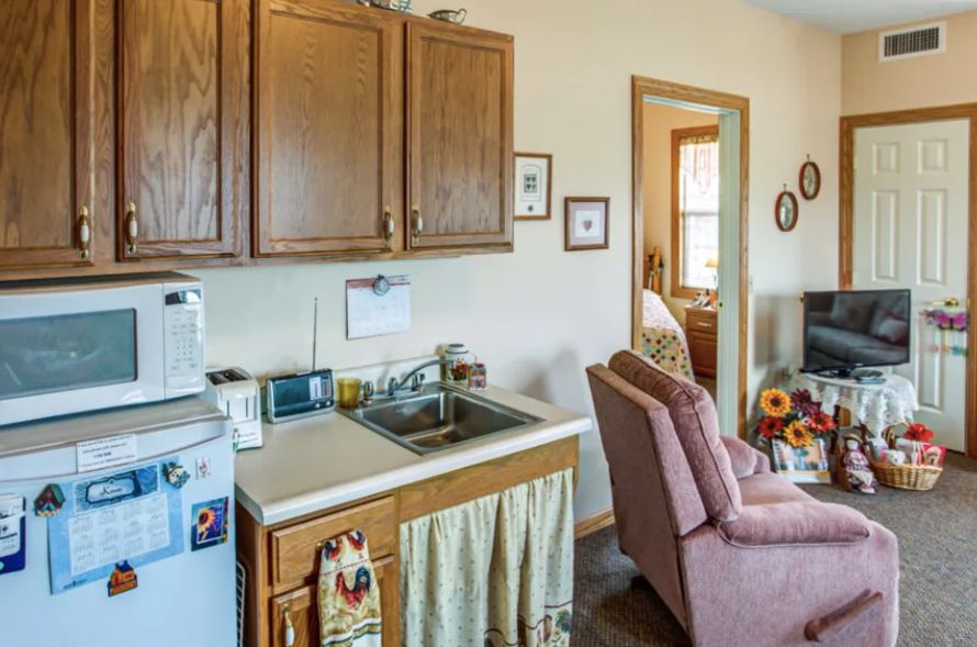 A cozy kitchen and living area featuring wooden cabinets, a sink, and a comfortable chair.