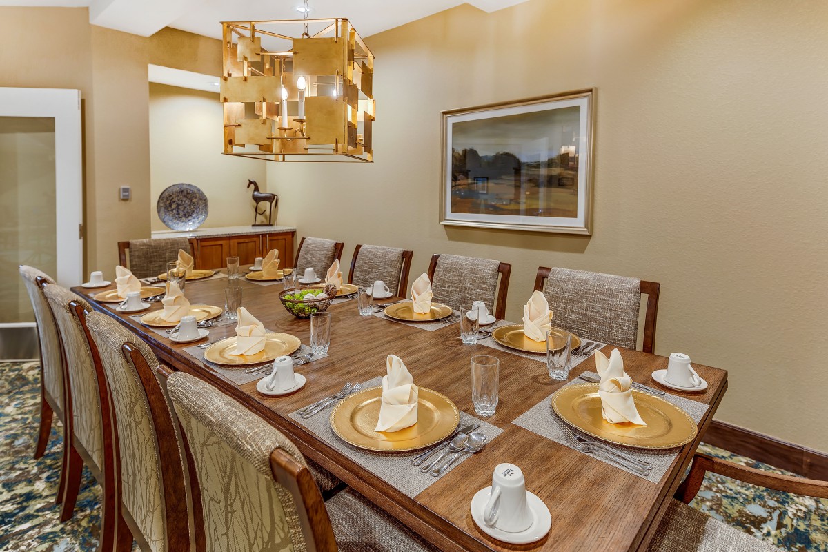 An elegantly set dining room with a long wooden table, ornate chandelier, and neatly folded napkins on each place setting.