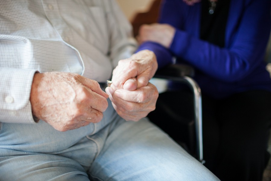 An elderly person in a wheelchair being cared for, with a focus on their hands.