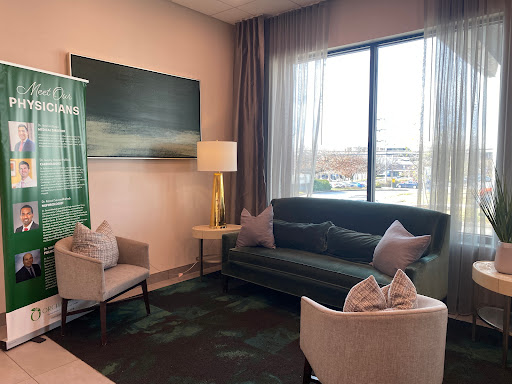 A cozy and modern lounge area featuring a dark green sofa, light-colored armchairs, and large windows that let in natural light.