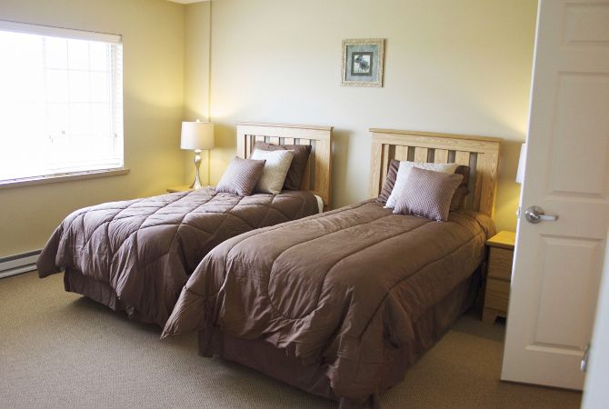A cozy bedroom featuring twin beds with matching bedding and wooden headboards, complemented by a bedside lamp and soft lighting.