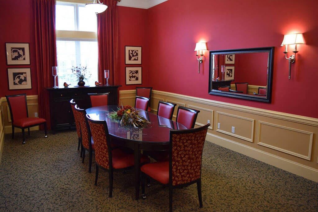 A formal dining room with red walls and matching chairs, featuring a large mirror and decorative wall art.