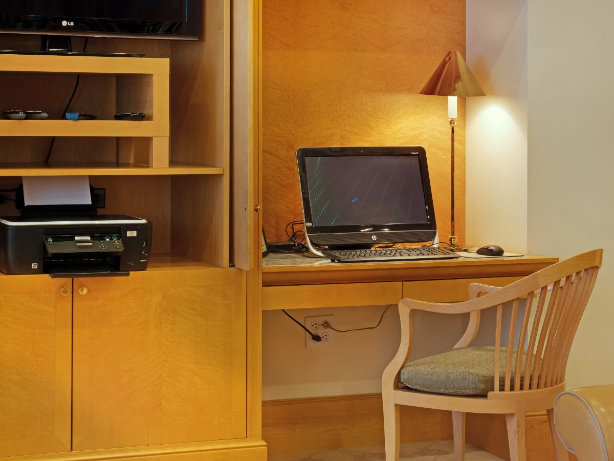 A compact workspace featuring a computer desk with a chair and a lamp, along with adjacent shelving housing a printer.