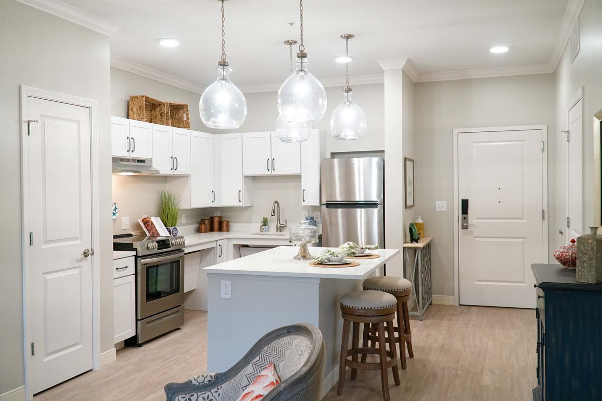 A modern kitchen featuring white cabinets, an island with bar stools, and stainless steel appliances under pendant lighting.
