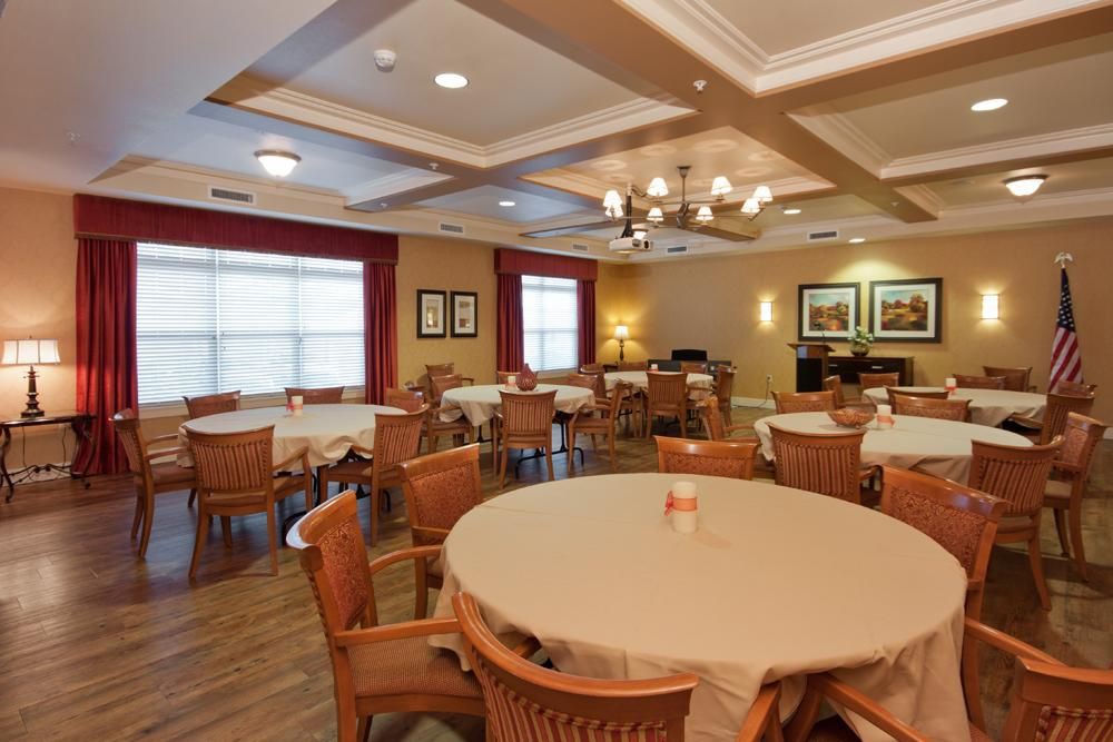 A warmly lit dining room with multiple tables and chairs arranged neatly beneath a chandelier.