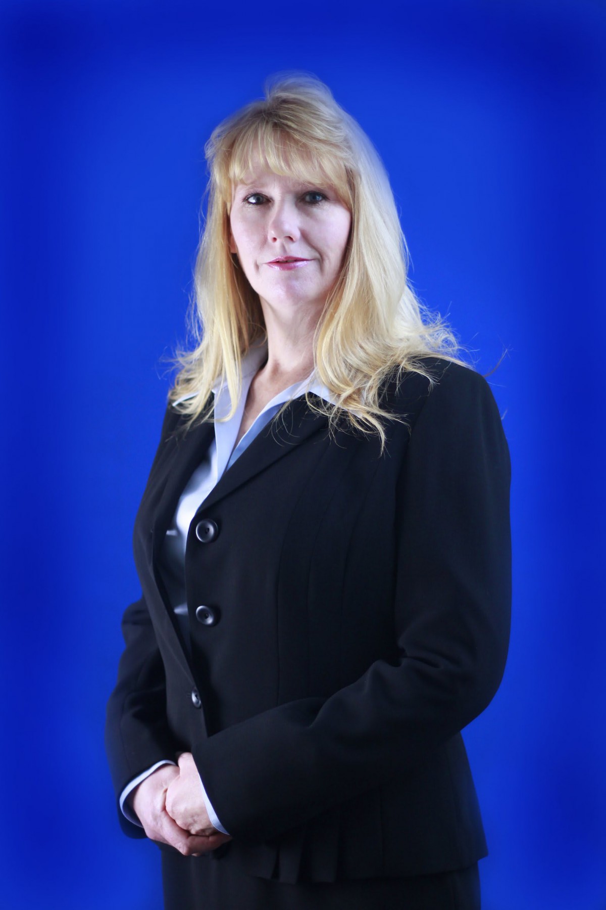 A professional portrait of a woman in a business suit standing against a blue background.