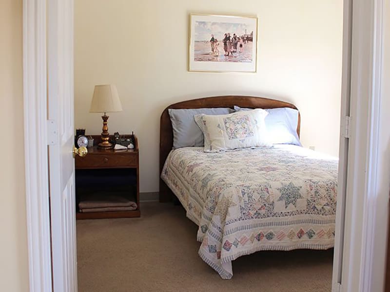 A cozy bedroom with a single bed, nightstand, and lamp.
