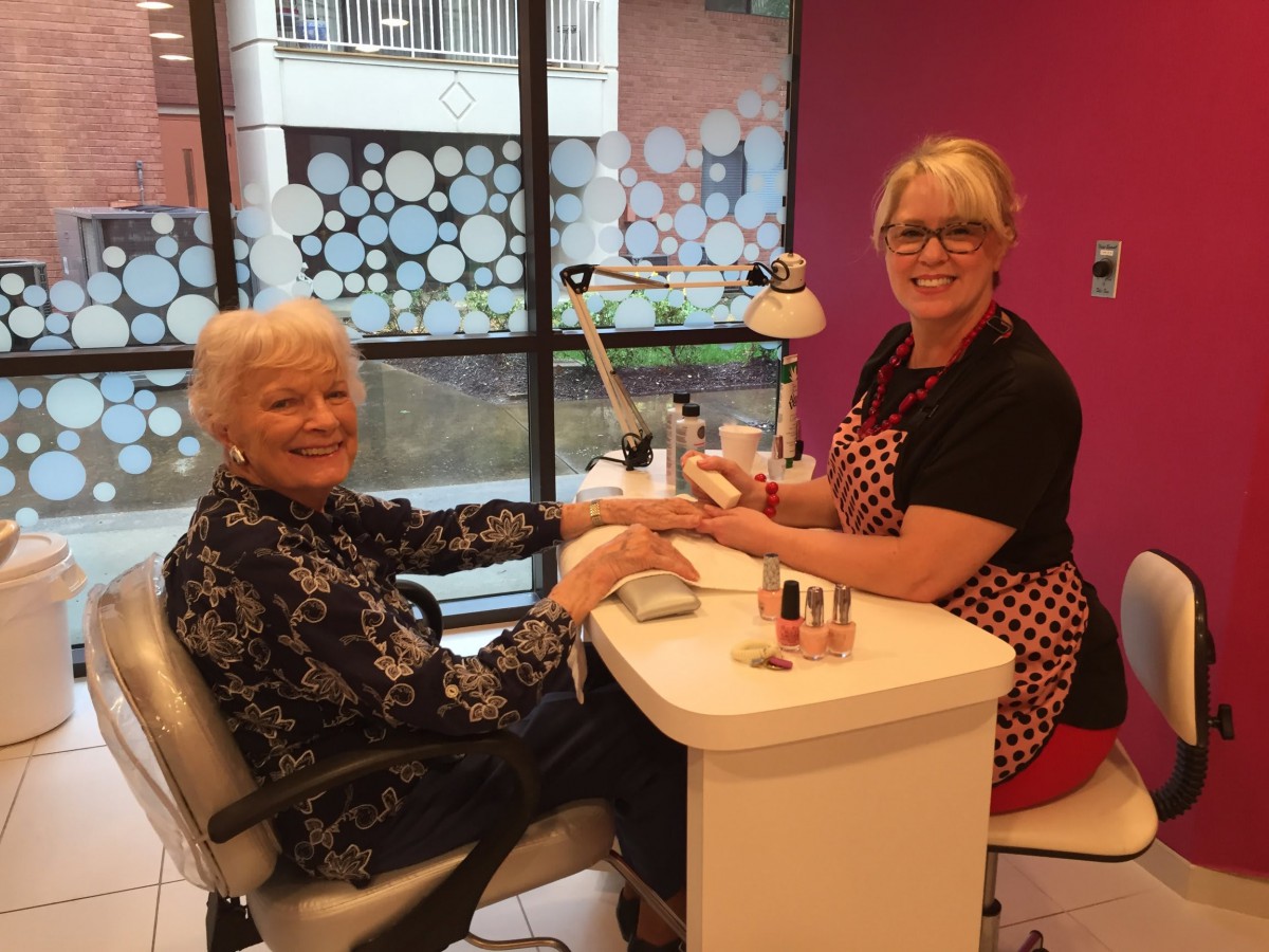 An elderly woman receives a manicure from a nail technician in a salon setting.