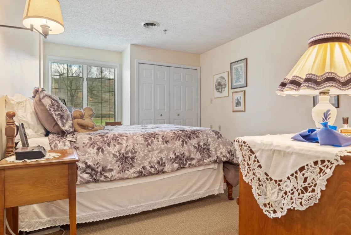 A cozy bedroom with a neatly made bed, decorative furnishings, and ample natural light from the window.