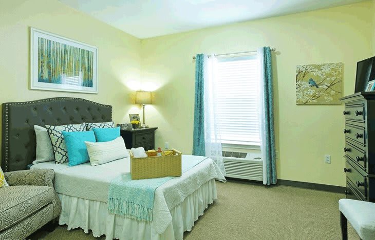 A cozy and well-decorated bedroom with a comfortable bed, bedside table, lamp, and window with curtains.