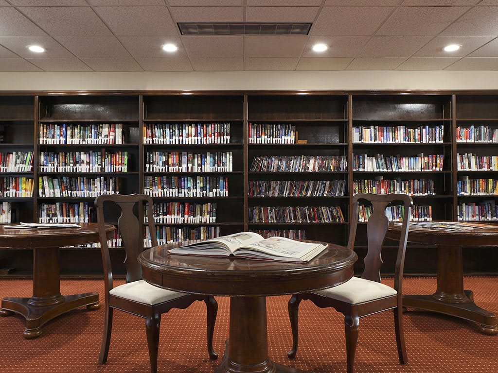 A cozy library reading area with a round table and chairs surrounded by bookshelves.