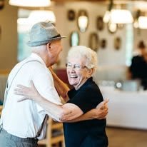 An elderly couple shares a joyful dance indoors, radiating happiness.