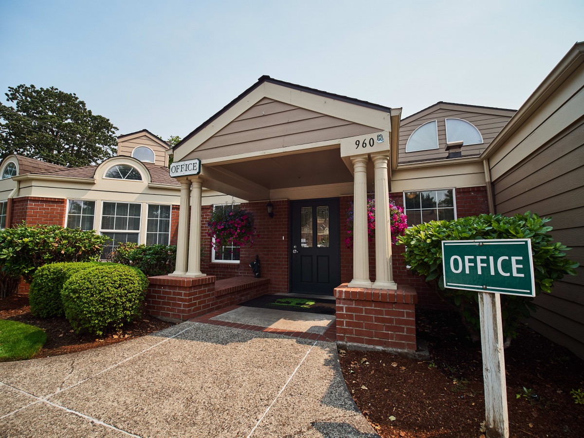 The entrance to a brick office building with columns and surrounding greenery.