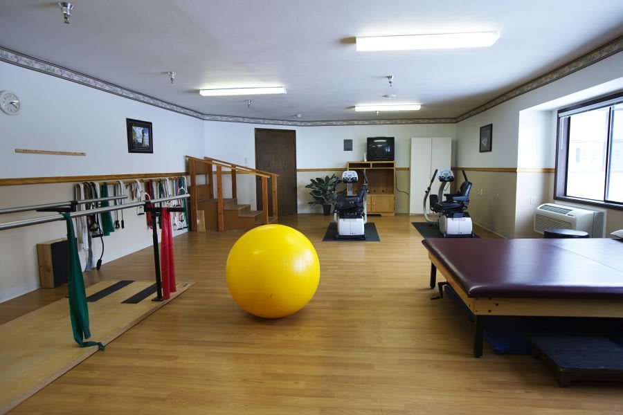A rehabilitation center with various exercise equipment and a large yellow therapy ball.