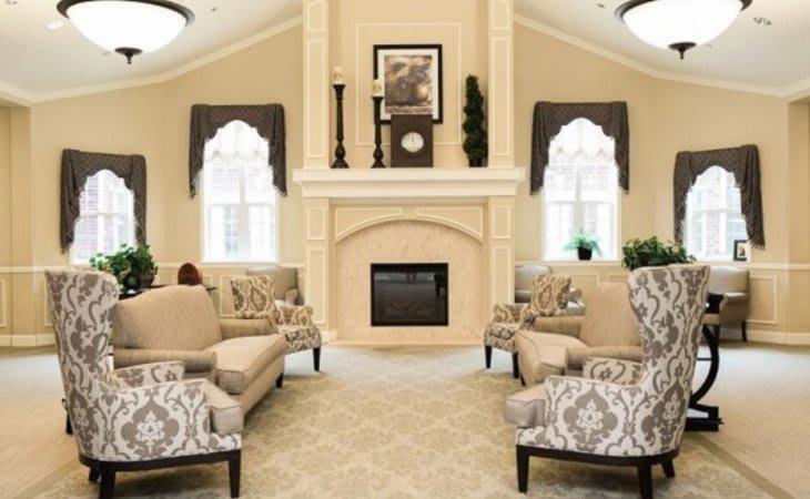 An elegantly designed living room featuring a central fireplace, patterned seating, and large windows with draped curtains.