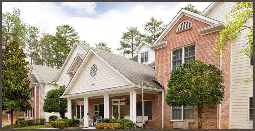 A charming suburban house with a brick facade and a welcoming porch surrounded by trees.