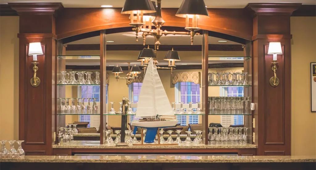 An elegant bar interior featuring a model sailboat displayed on shelves surrounded by wine glasses.