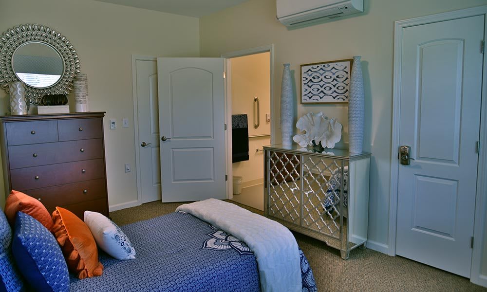 A cozy bedroom featuring a neatly made bed with blue bedding, a decorative dresser with a mirror on top, and an open door leading to another room.
