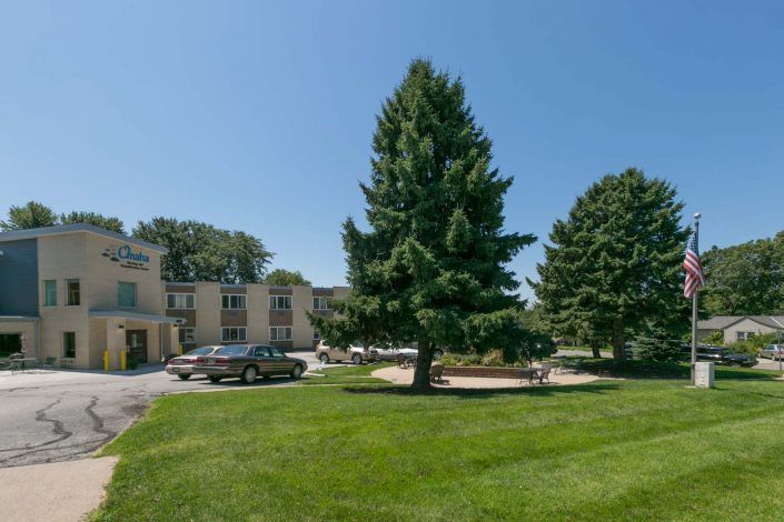 A building with a large tree and car in front, set on a sunny day.