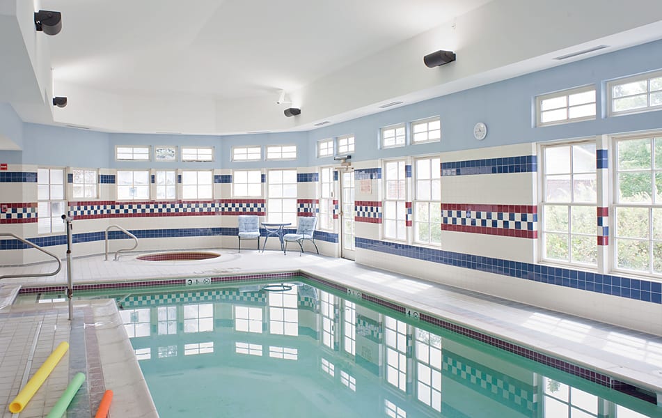Indoor swimming pool with a jacuzzi and tiled walls, illuminated by natural light from large windows.