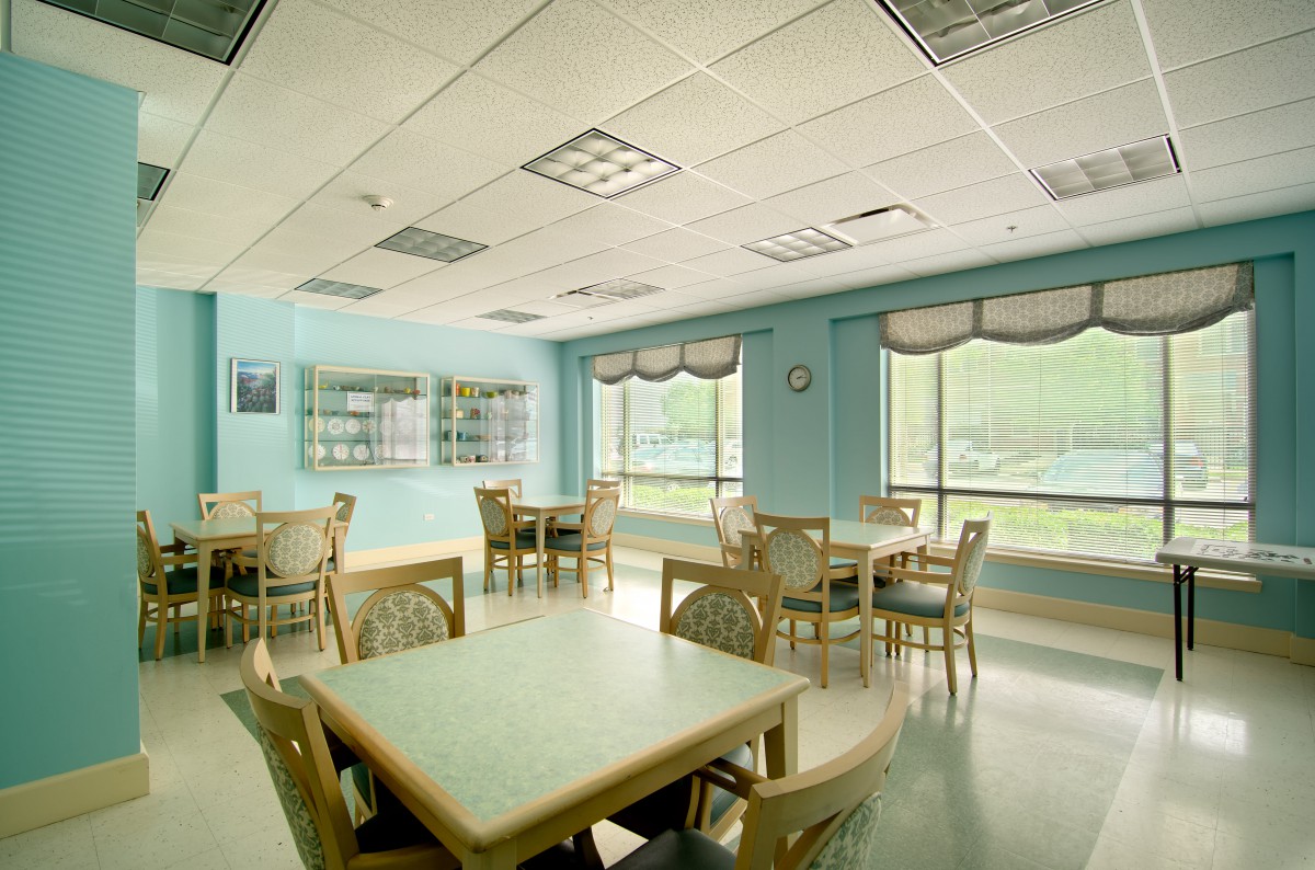 An empty dining room with multiple tables and chairs, illuminated by natural daylight through large windows.