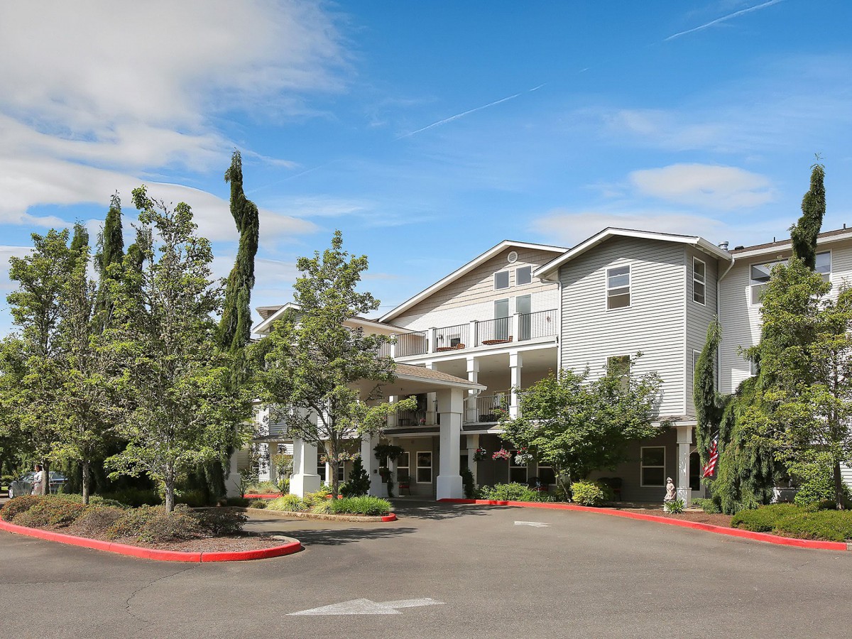 A residential building surrounded by trees under a blue sky.
