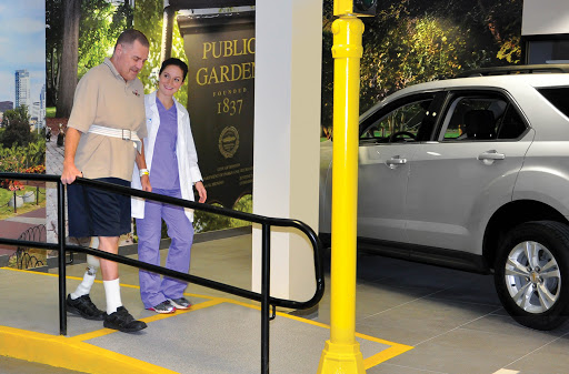 A nurse assists a patient as they walk towards a vehicle in a hospital parking area.