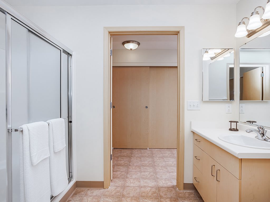 A modern bathroom featuring a glass shower, mirrored vanity, and tile flooring.