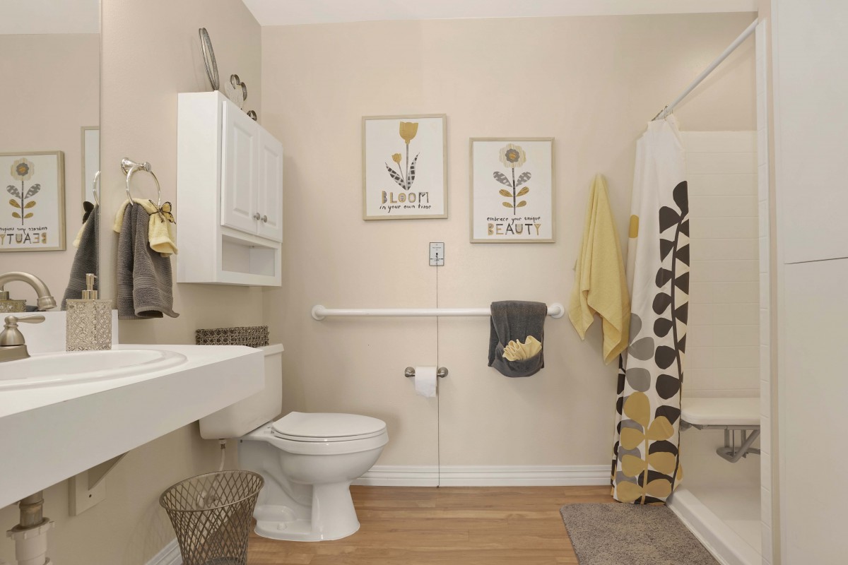 A modern bathroom featuring a toilet, sink, and shower area with decorative artwork and towels.