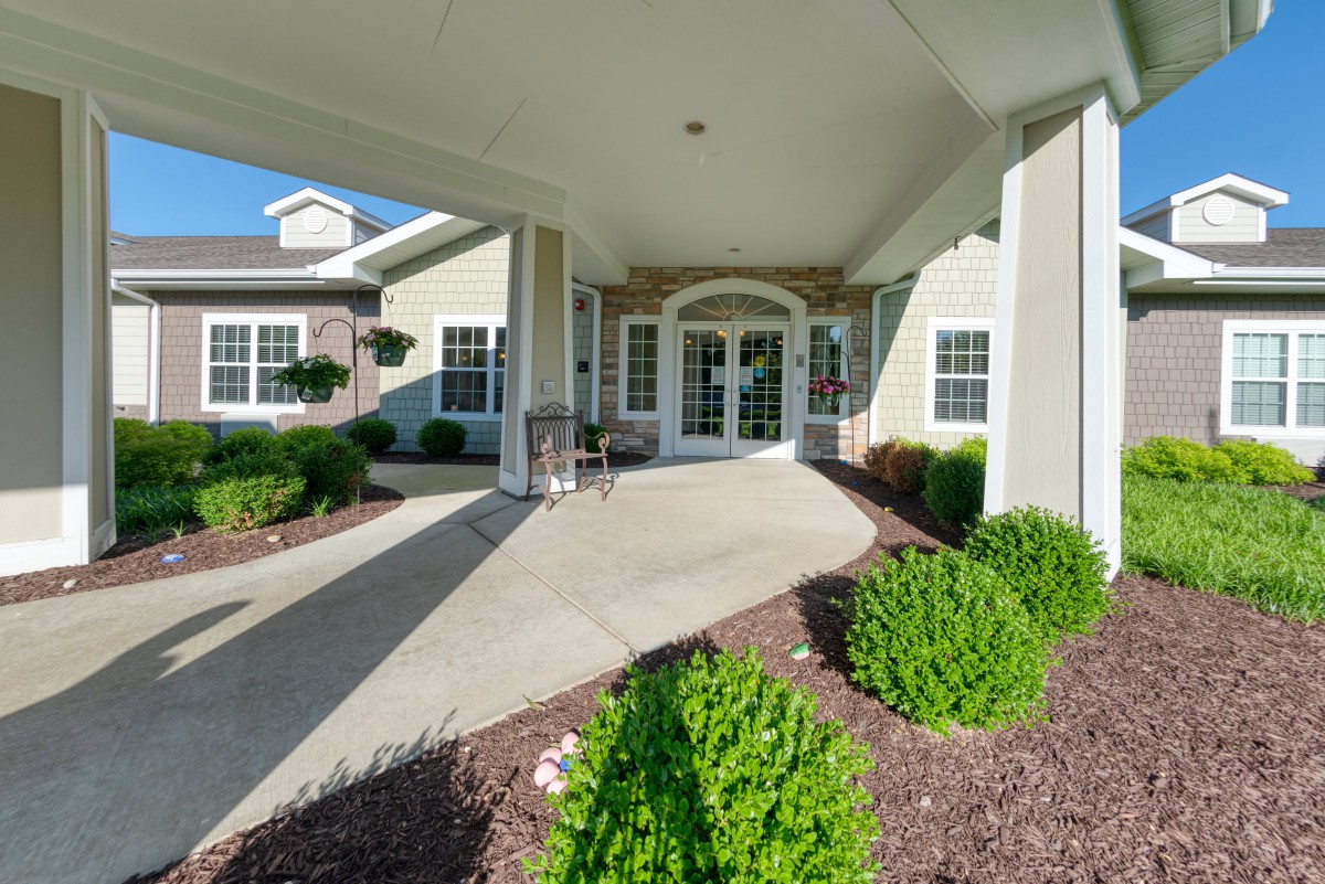A neatly landscaped building entrance with a covered walkway and well-maintained shrubs.