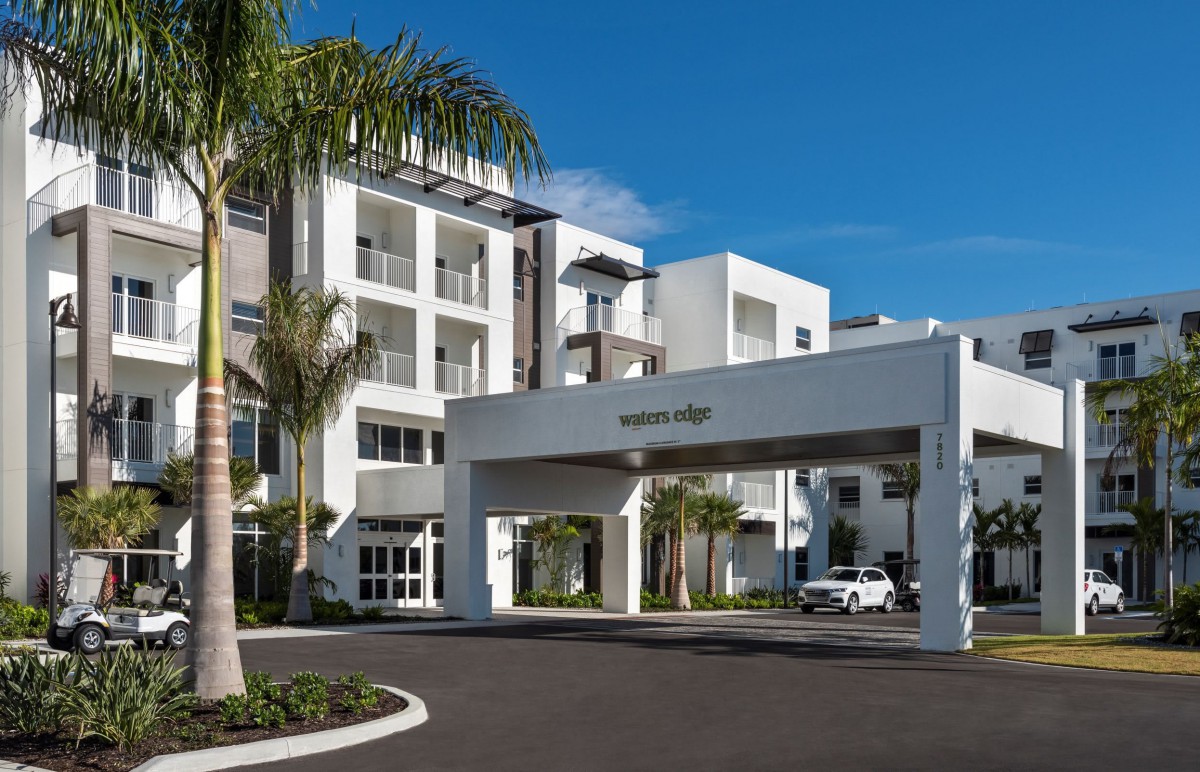 A modern apartment complex with palm trees and a welcoming entrance under a clear blue sky.