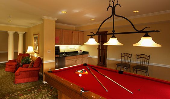 A cozy billiard room with a red pool table and warm ambient lighting.