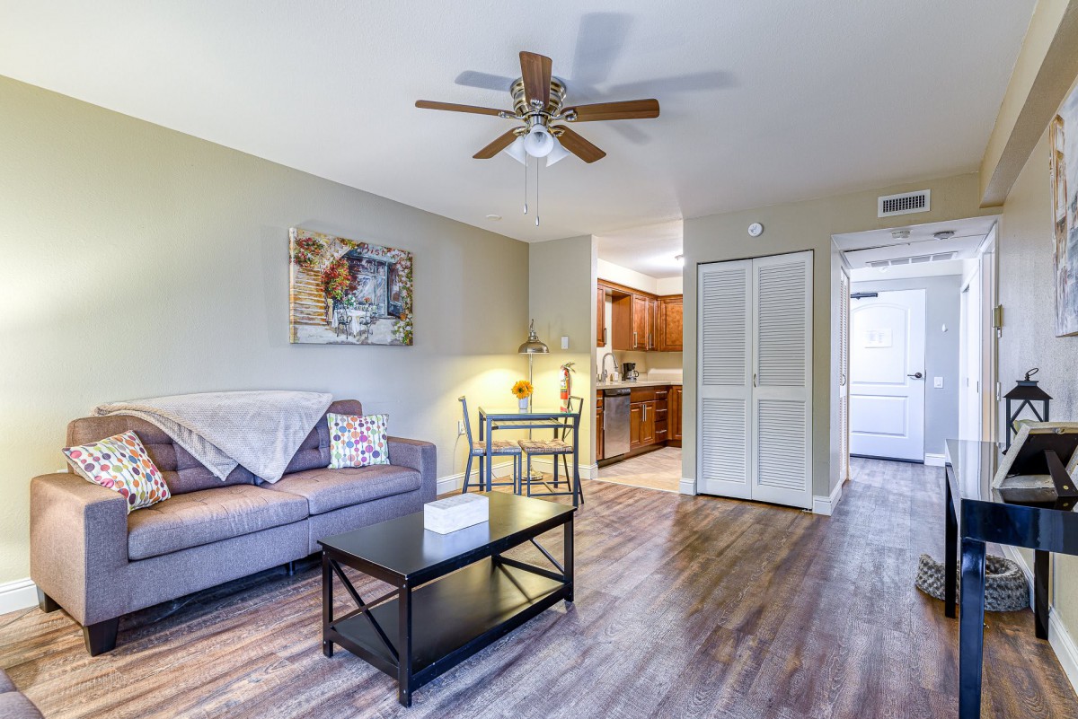 A cozy living room with a sofa, coffee table, and ceiling fan, featuring an adjacent kitchen area.
