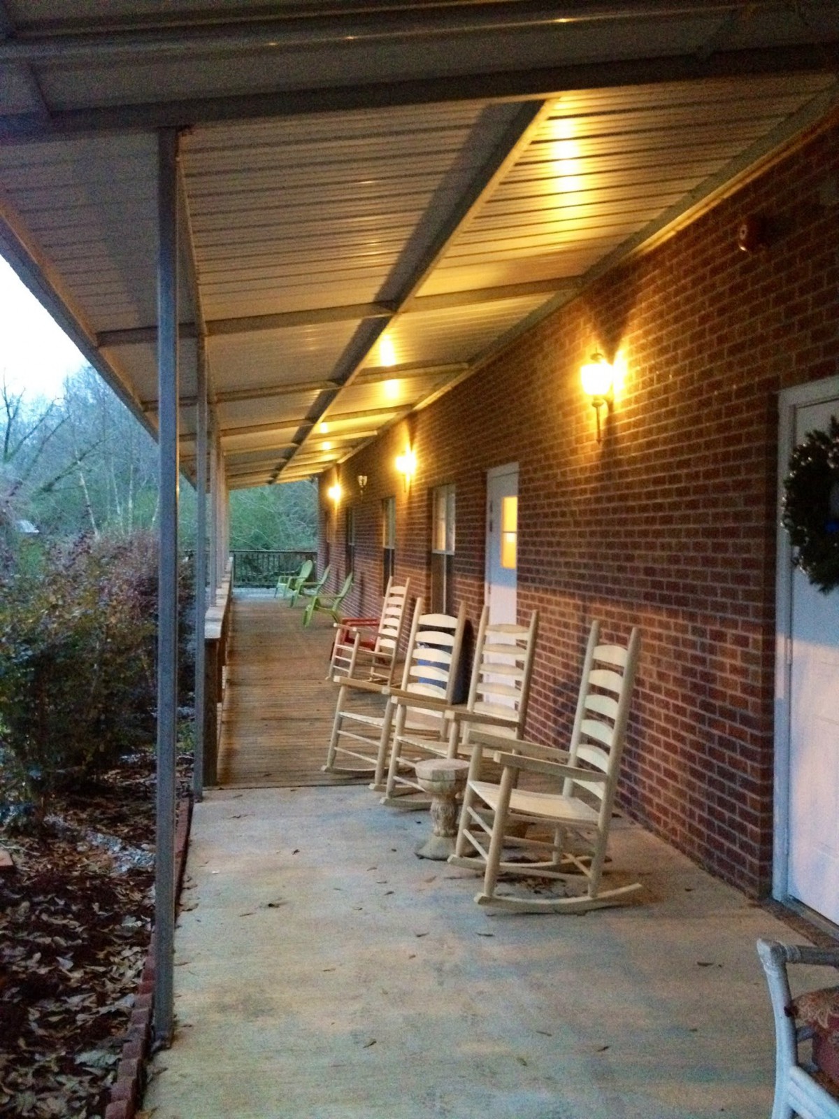 A cozy porch with rocking chairs lined up along a brick building, illuminated by warm outdoor lights.