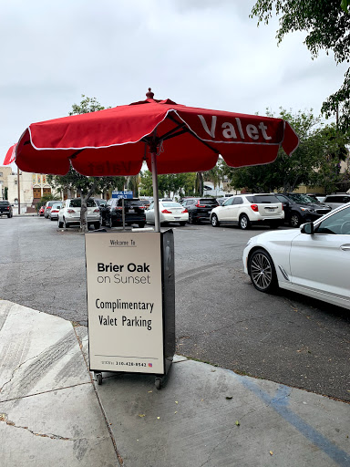 A valet service sign offering complimentary parking, situated under a red umbrella on a city street.