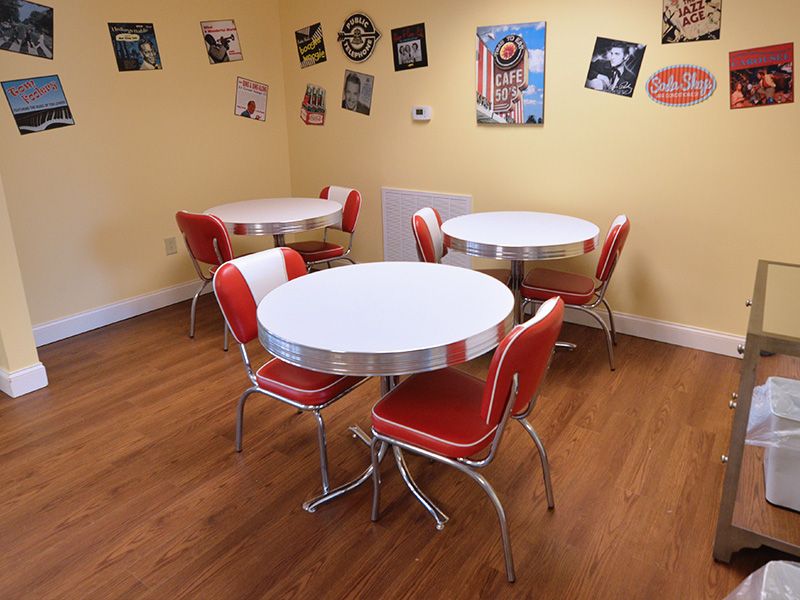 A retro diner setting with red chairs and round tables, adorned with vintage wall decor.
