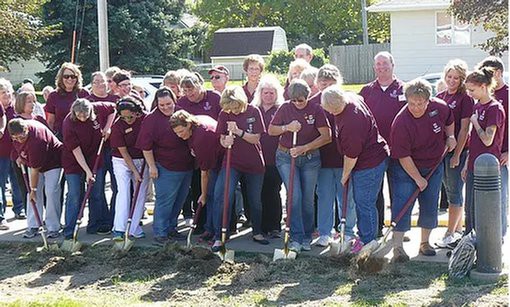 A group of people participating in a groundbreaking ceremony using shovels outdoors.