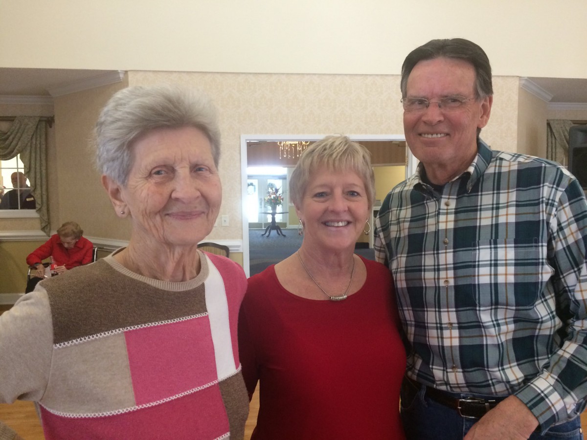 Three people standing together indoors, smiling at the camera.