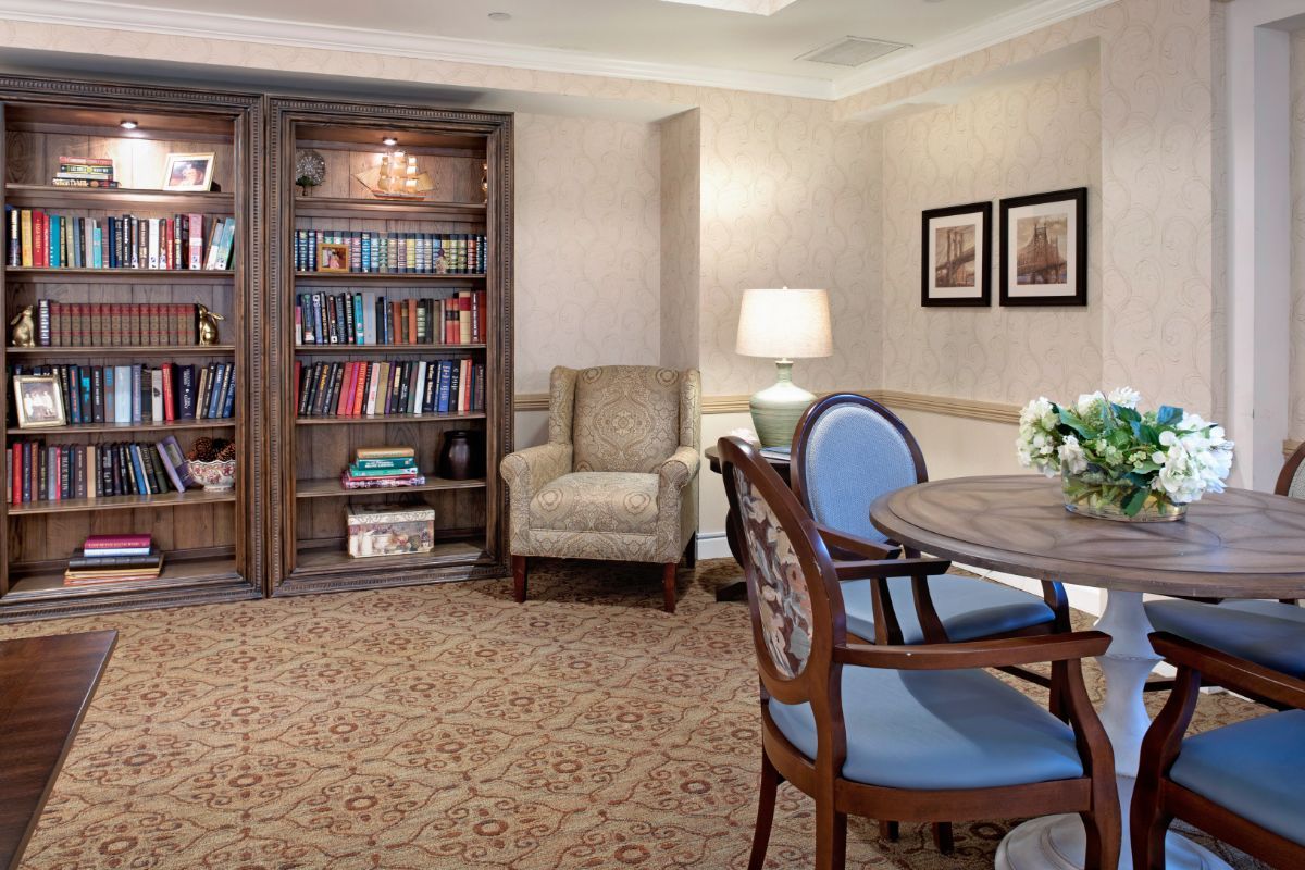 A cozy library room with a bookshelf, armchair, and table seating.