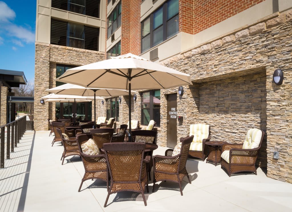 An outdoor patio area with wicker furniture and large umbrellas, adjacent to a building with a brick exterior.