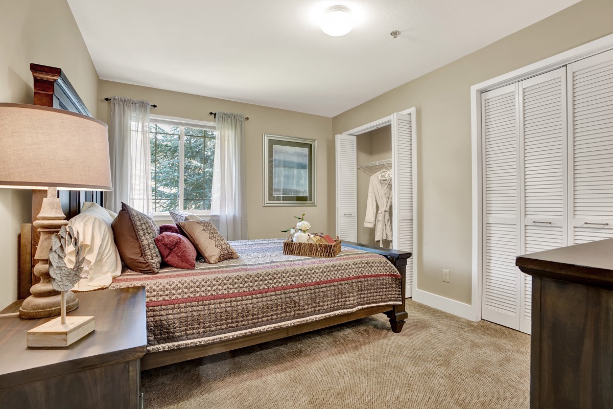 A cozy bedroom with a neatly made bed, soft carpeting, and natural light from the window.