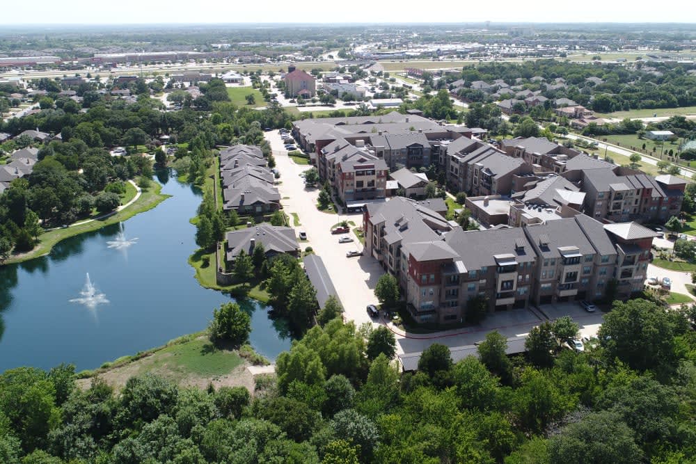 Aerial view of a residential area with modern buildings, surrounded by greenery and a water body.