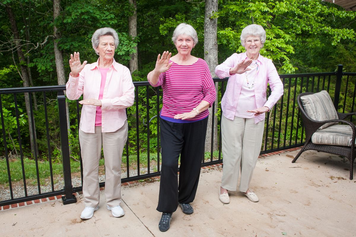 Three elderly women practicing Tai Chi outdoors in a park.