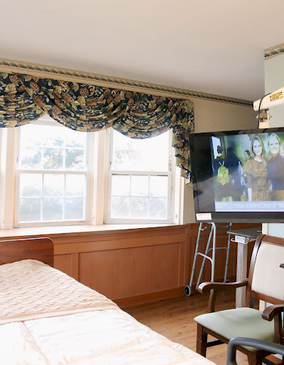 A well-lit hospital room featuring a bed, window with decorative curtains, and a television.