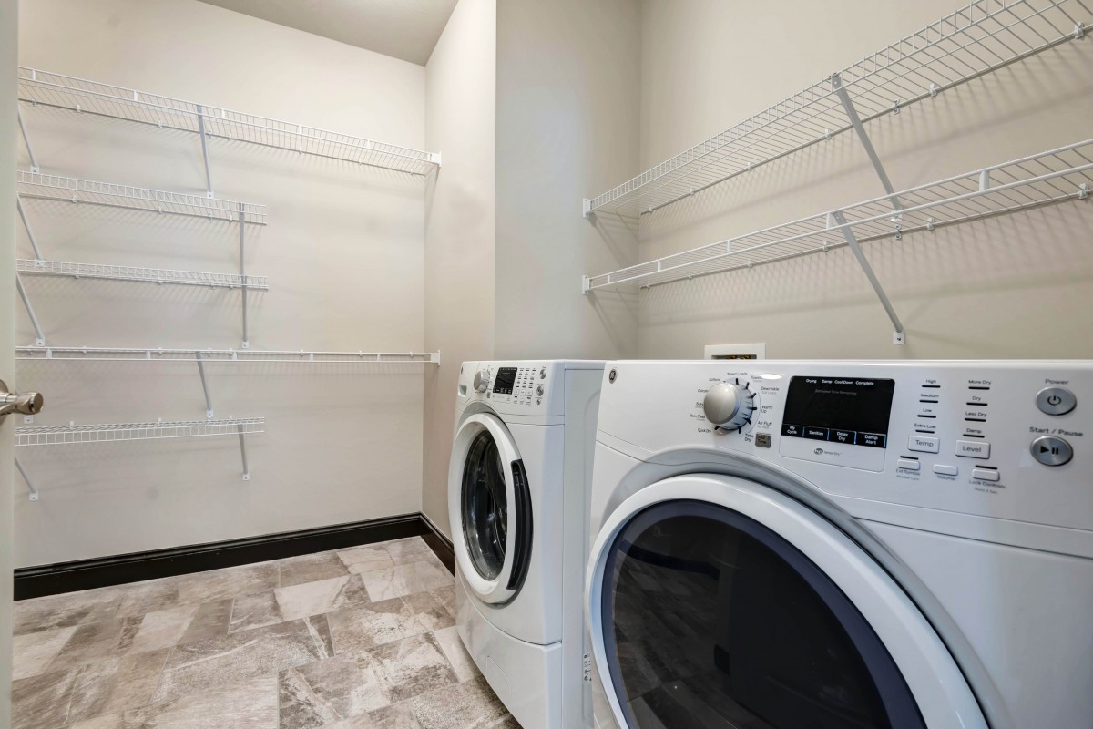 A modern laundry room featuring a washer and dryer with ample shelving space.