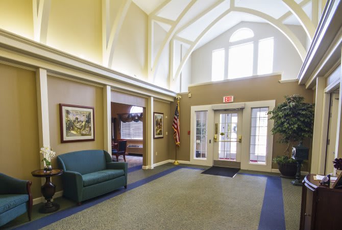 A well-lit lobby with a vaulted ceiling, featuring a sofa, artwork on the walls, and an entrance area.