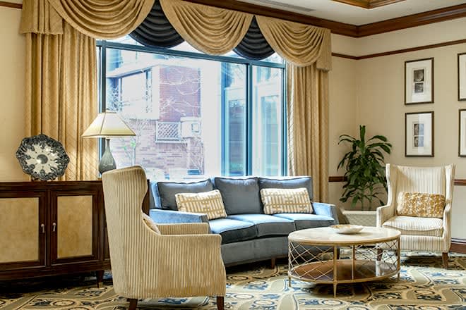 A cozy living room with elegant furnishings, featuring a sofa, armchair, coffee table, and large window with decorative curtains.