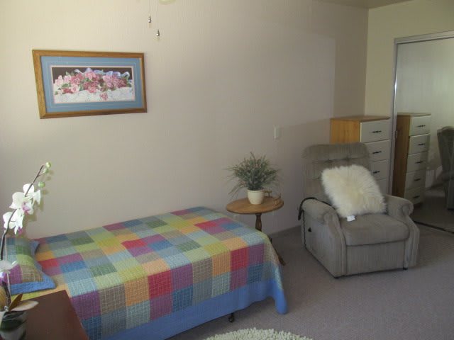 A cozy bedroom with a colorful quilt, reclining chair, and decorative elements.
