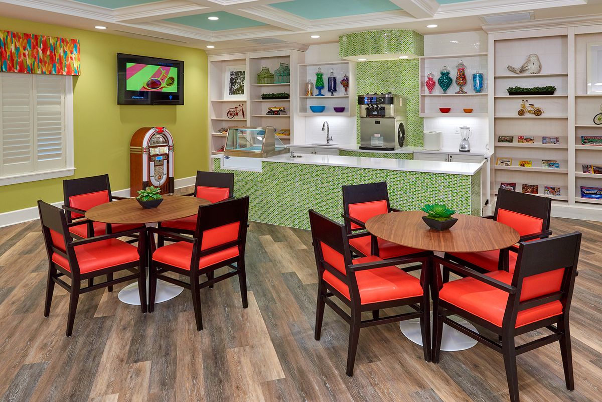 A vibrant cafe interior featuring colorful chairs, round tables, a jukebox, and a counter with various decorations.